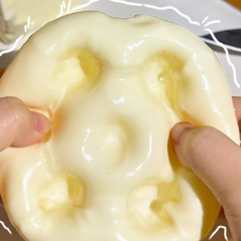 Hands squeezing the squishy cheese cube stress toy flat to show how soft it is